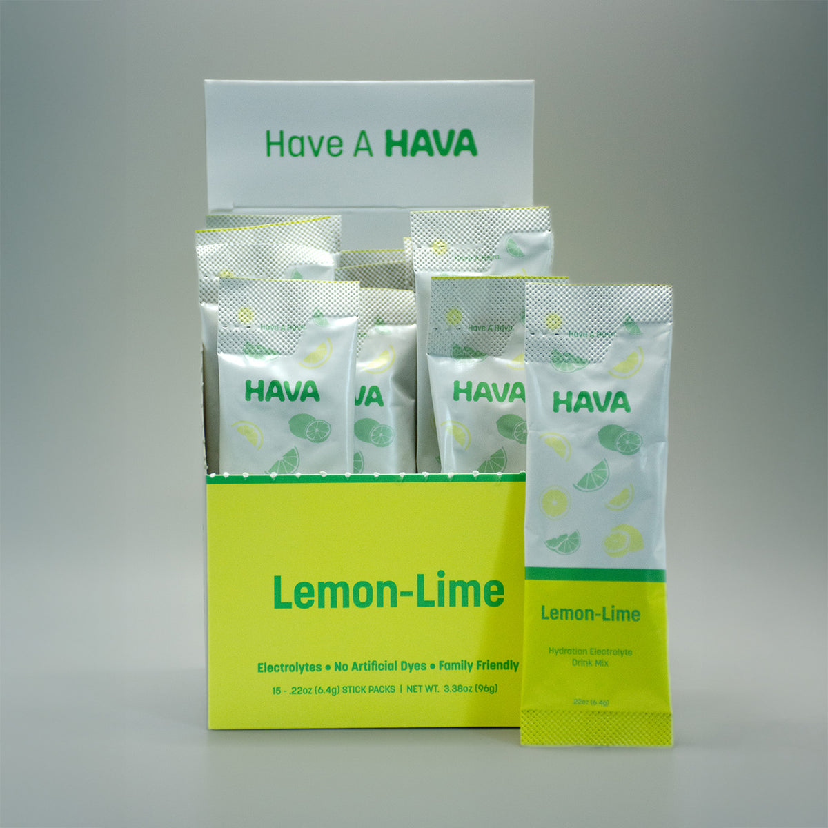 A display box and individual sachet of HAVA Lemon-Lime electrolyte packets on a neutral gray background. The packaging features a bright yellow-green base with white and green graphics depicting sliced lemons.